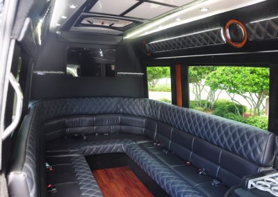 The interior of a limo shuttle features a black sofa with built-in water bottle holders