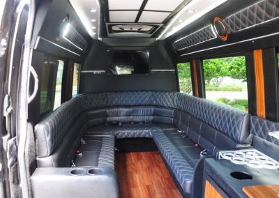 The interior of a limo shuttle features a black sofa with built-in water bottle holders