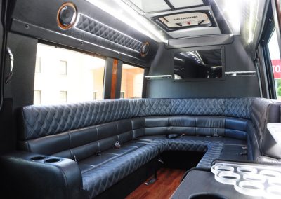 The interior of a limo shuttle features a black sofa with built-in water bottle holders