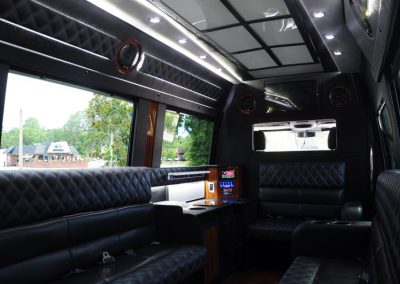 The interior of a limo shuttle features a black sofa with built-in water bottle holders and a mini TV setup