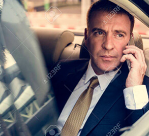 A man in suit and tie sitting inside of car speaking in phone. Luxury transportation services in Jacksonville FL offered by SD Transportation